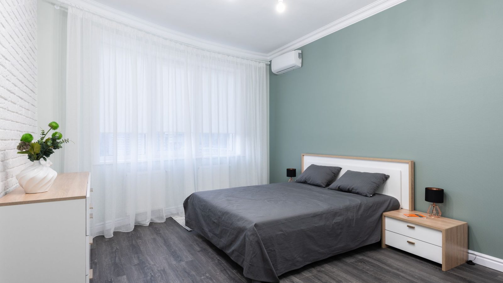 Chambre adulte aux murs bleu-gris doux, lit gris, rideaux blancs et table de chevet en bois clair