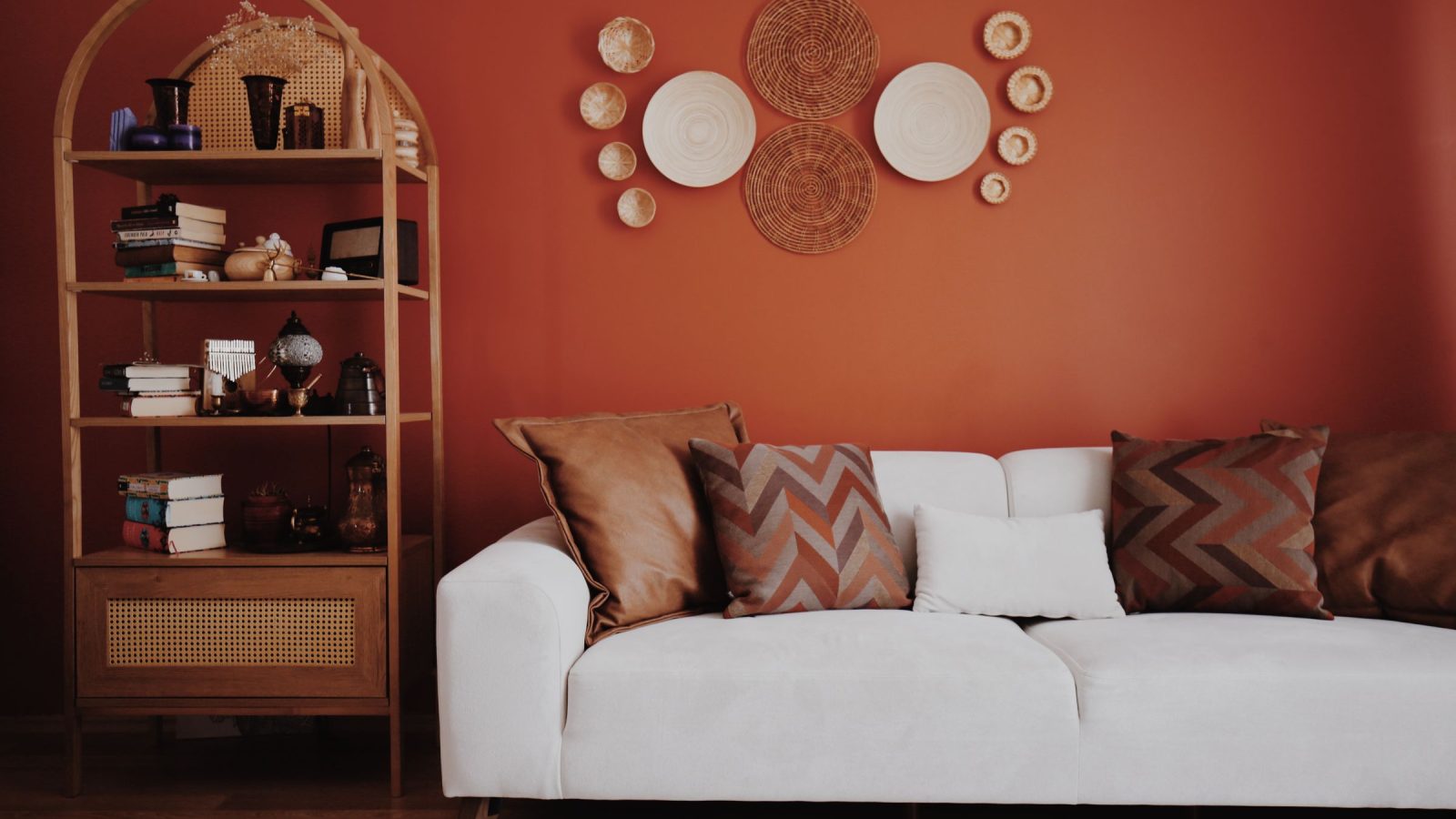Salon avec un mur terracotta, une étagère en rotin, des assiettes décoratives et un canapé blanc