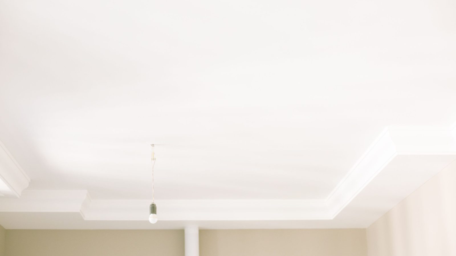 Plafond blanc lumineux avec corniche, une ampoule suspendue au fil et des murs beiges