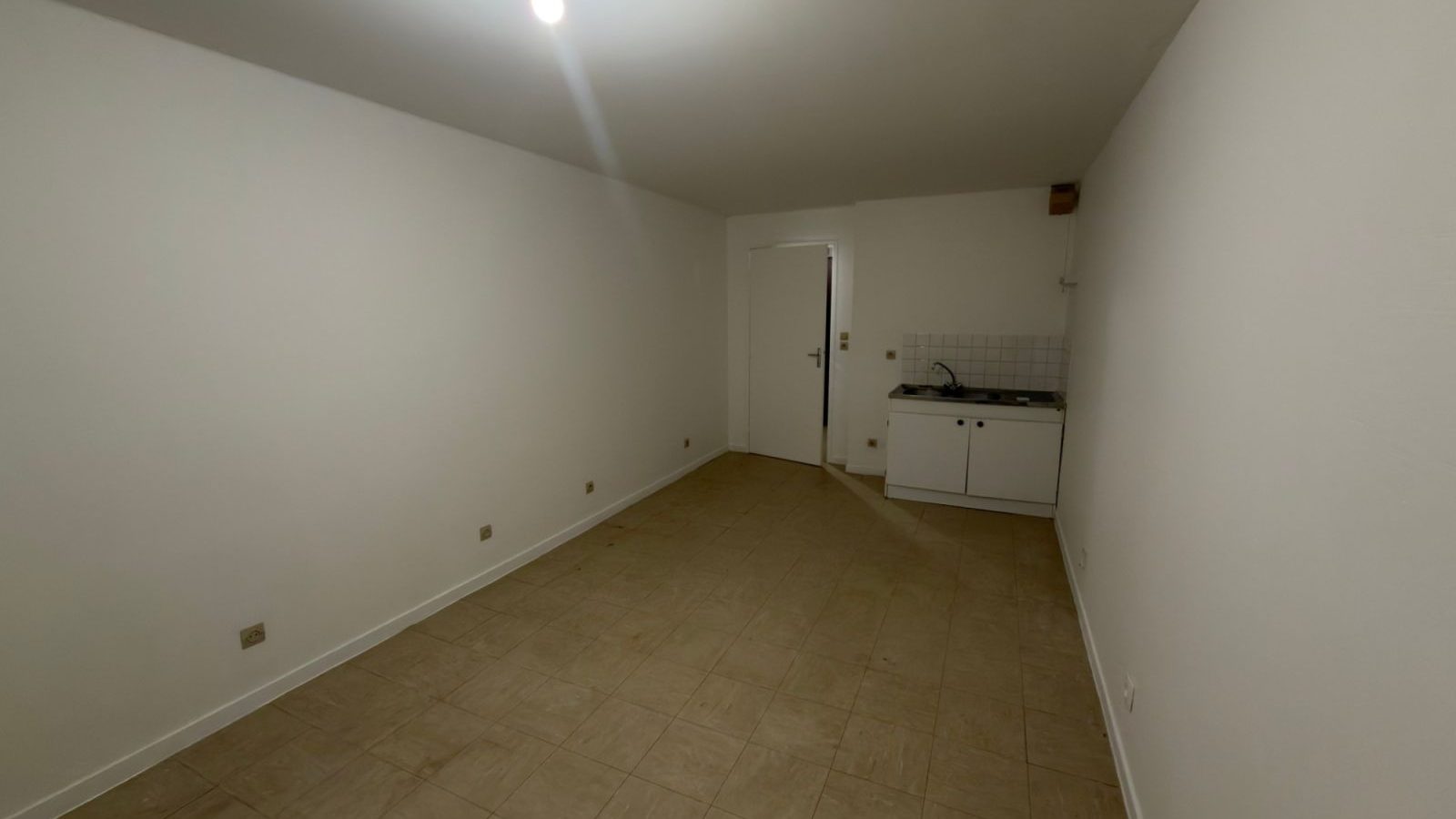 Studio en Yvelines après rénovation : pièce vide aux murs blancs et sol carrelé, kitchenette au fond