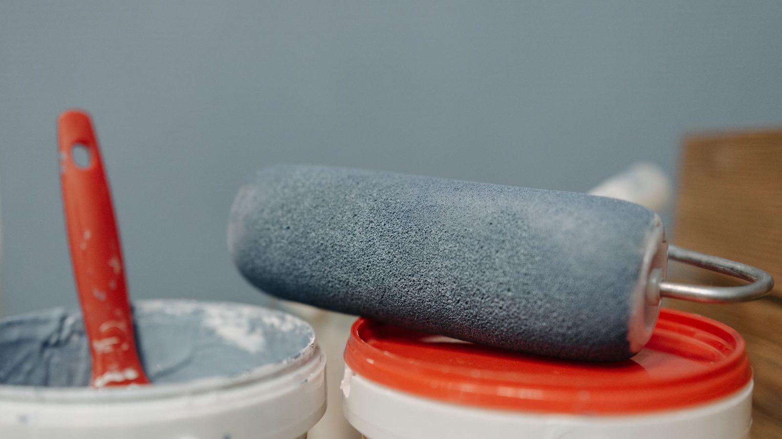 Rouleau gris posé sur un pot de peinture à couvercle rouge, à côté d'un pot ouvert avec un pinceau rouge