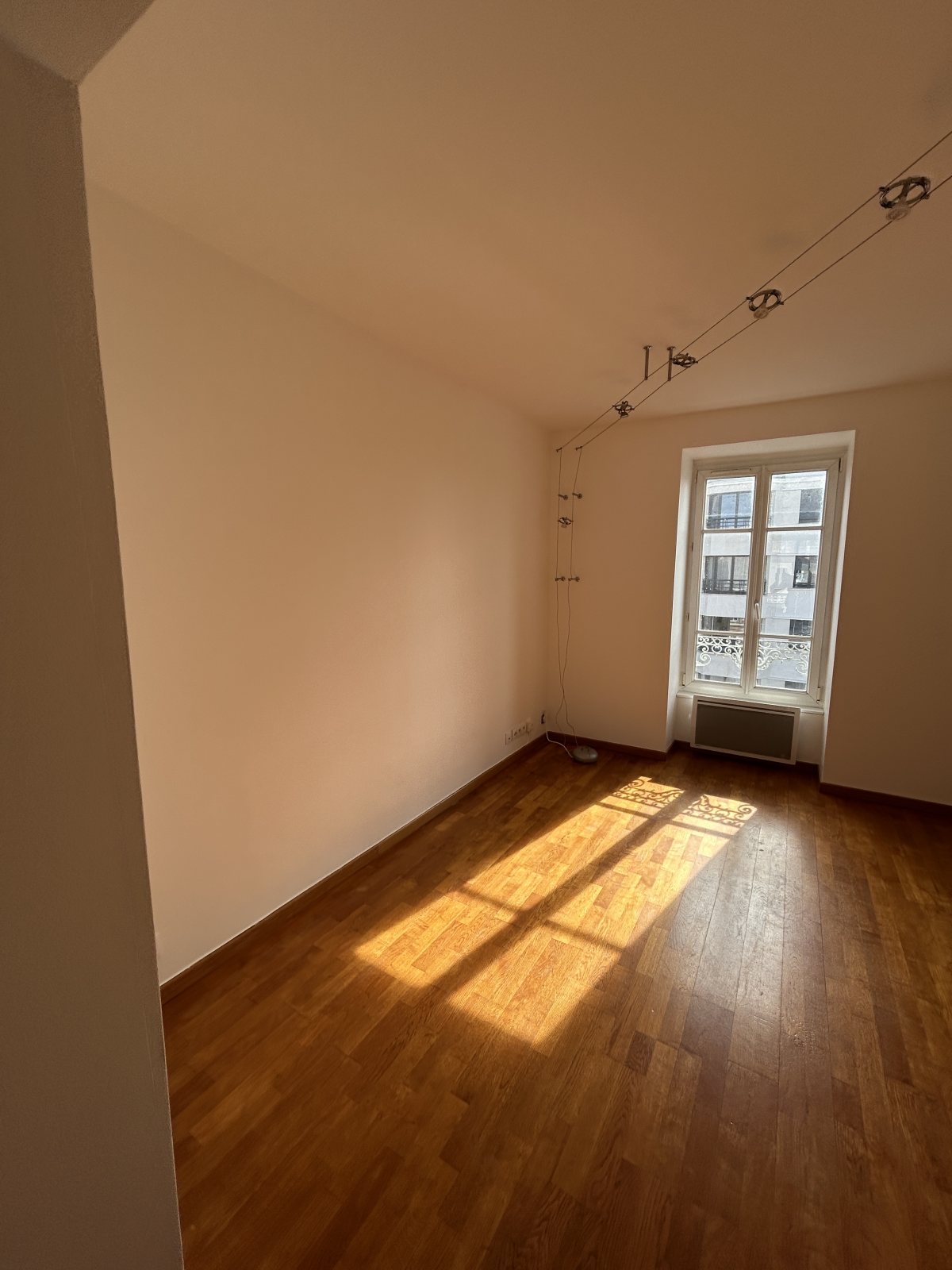 Pièce repeinte en blanc, fenêtre ensoleillée, câbles d'éclairage et parquet bois foncé - Yvelines